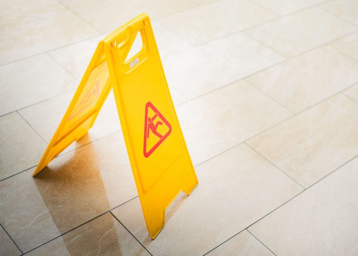 A bright yellow caution sign on a tiled floor indicates a wet surface, alerting passersby to potential hazards.